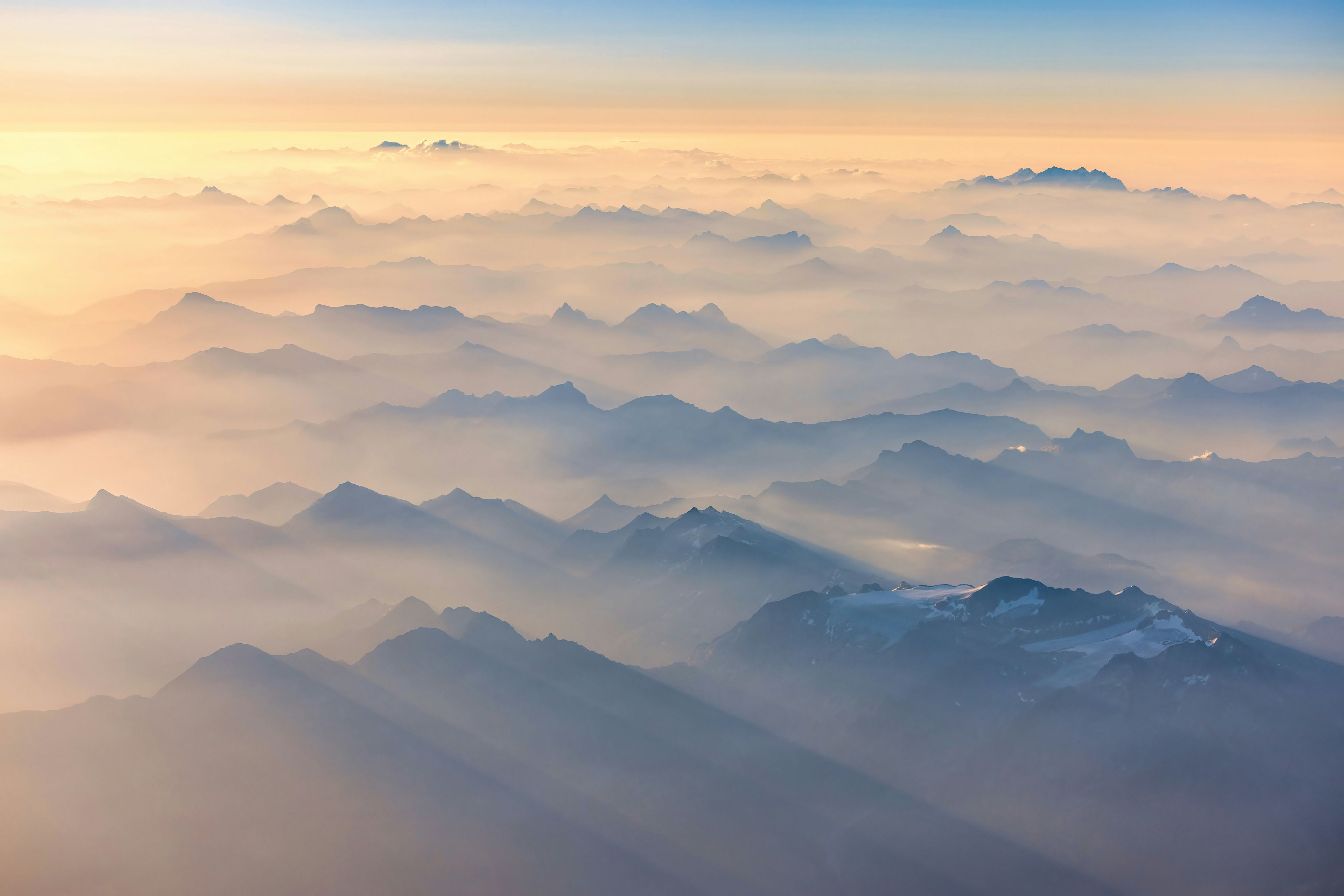 Mountain range peaks emerge from clouds at sunrise.